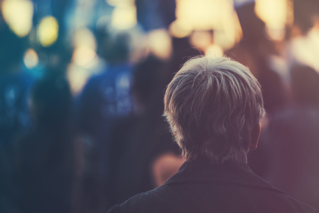 Aging population. Unrecognizable older adult person on outdoor political meeting from behind, looking toward gathered crowd and stage.