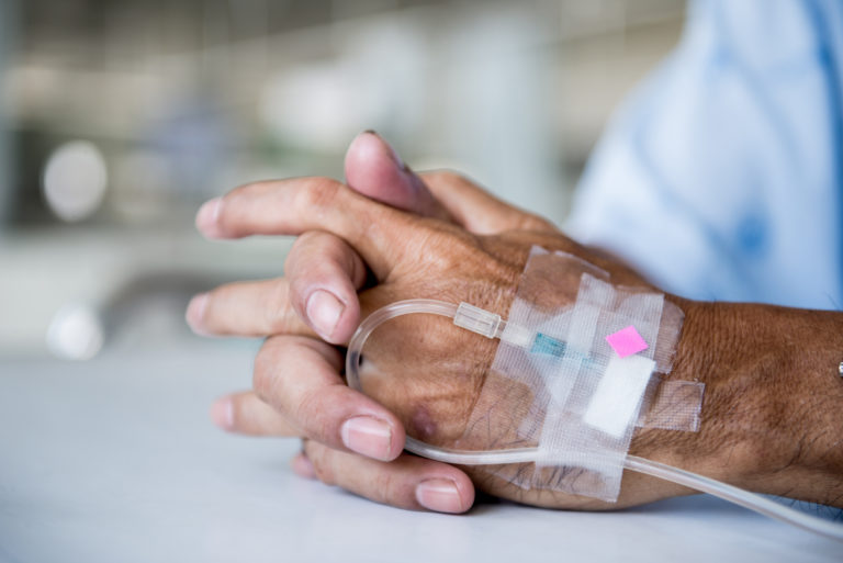 Annuities. Hands of an older person in the hospital with an IV drop in