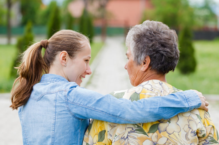 Shot from behind of elderly woman walking with her young female caregiver