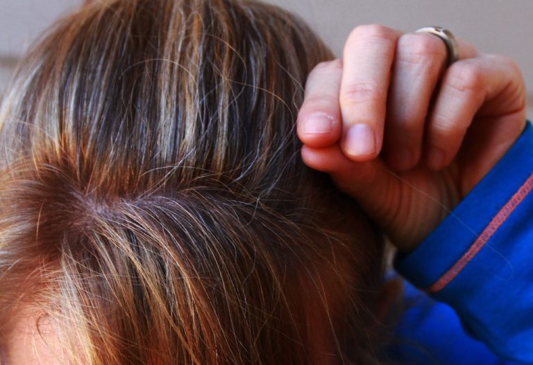 Shot of top of brunette woman's head while she pulls on piece of gray hair