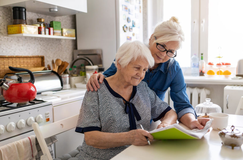 Caregiver helping senior with Alzheimers write in a notebook