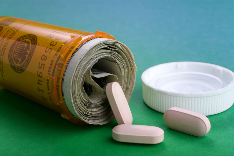 Healthcare concept: Money filling perscription bottle with only a few pills spilling out. Represents rising cost in healthcare costs.