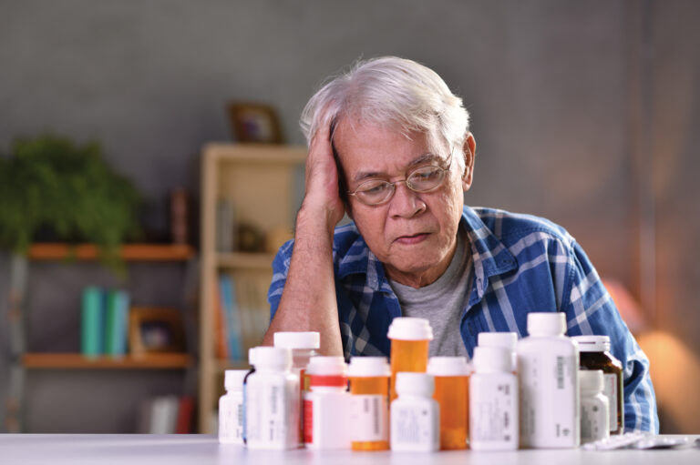 Senior with many medicine bottles on a kitchen table representing drug reactions issue