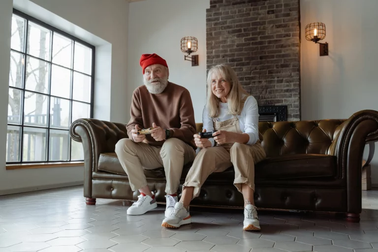 A man in a red hat and a woman with long hair sit together on a brown leather couch playing video games.