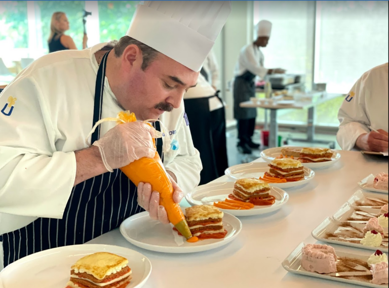 A chef pipes an orange puree onto a plate in a line of similar plates.