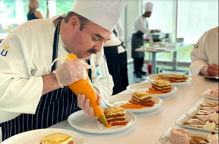 A chef pipes an orange puree onto a plate in a line of similar plates.