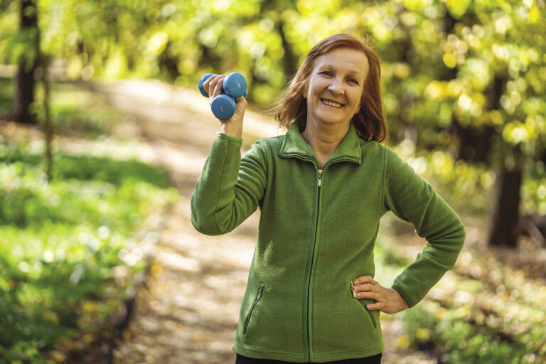 Exercise and fitness. Senior woman with small weights in her hand outdoors on a trail