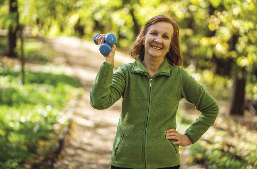 Exercise and fitness. Senior woman with small weights in her hand outdoors on a trail