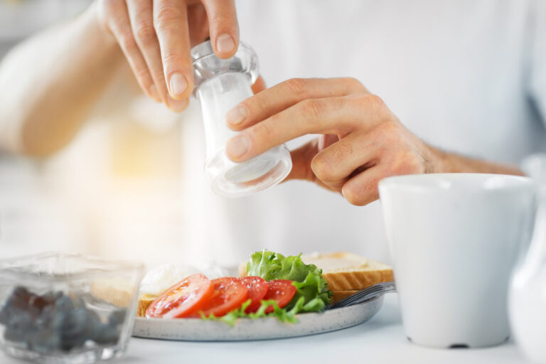 A close-up of hands holding a salt shaker over a plate of vegetables