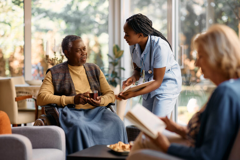 Black senior man in wheelchair drinks tea while talking to nurse. Chicago Commons services represented.