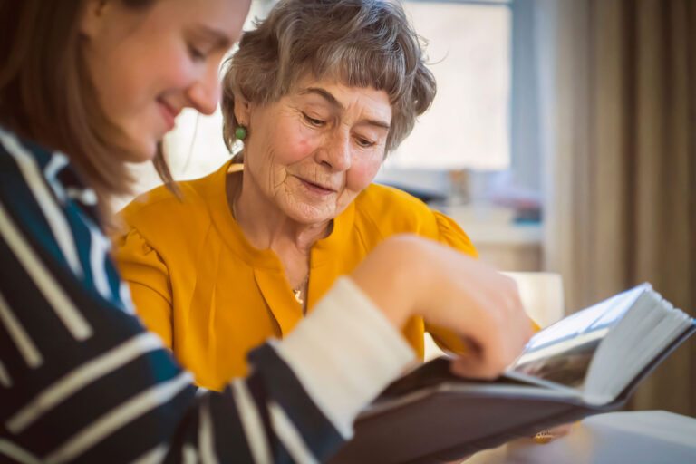 Two women sit together reading. They're smiling and looking down at the book.