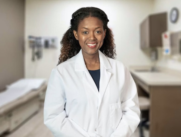 Physician Rene Roberts stands in her white coat in a patient room, smiling at the camera.