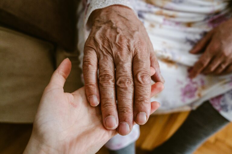 A younger hand holding a wrinkled, older hand.