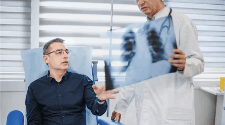 A middle-aged man looks at a chest x-ray with his physician, who is standing beside him holding up the x-ray scan