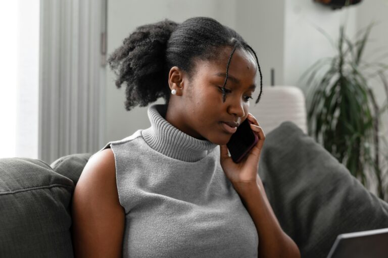 A woman in a gray sweater on the phone with a helpline.