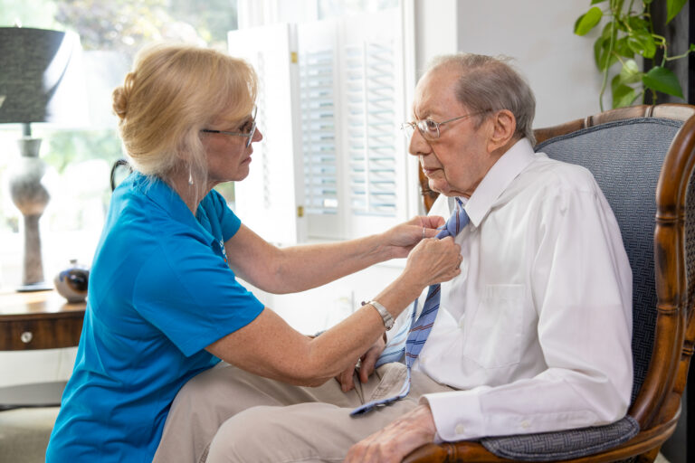 Caregiver puts a necktie on a senior man